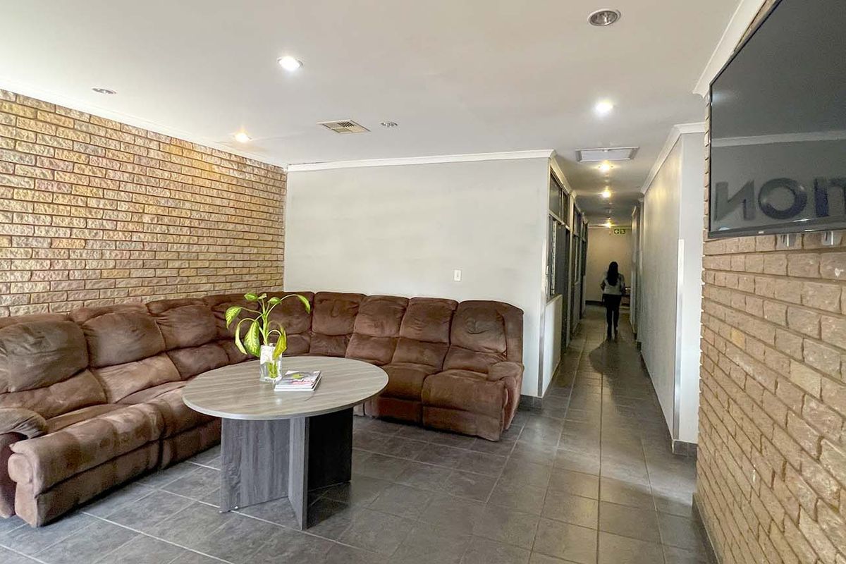 A spacious industrial-style waiting area or lounge featuring exposed brick walls, tiled flooring, and recessed ceiling lighting.