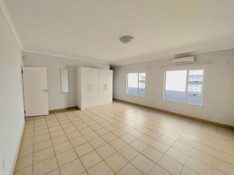 Spacious bedroom featuring neutral tiled flooring, built-in cupboards, and a wall-mounted air conditioning unit, offering a clean and functional living space.