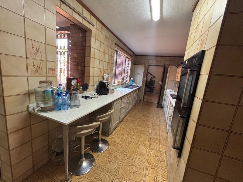 A functional kitchen featuring dated wall and floor tiles, built-in oven, and extended countertop space with a breakfast bar area.