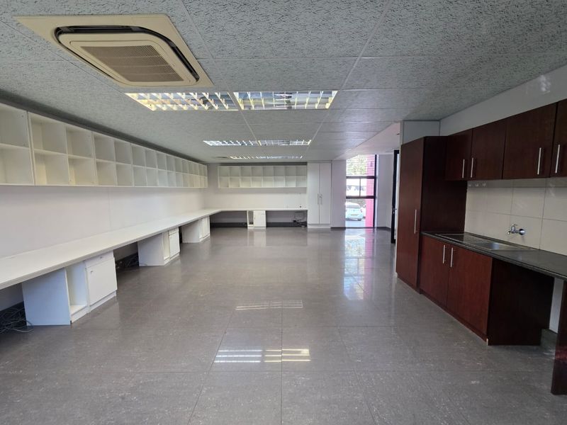 Spacious open-plan office featuring extensive built-in storage, integrated desk space, a kitchenette, tiled flooring, and modern recessed lighting with cassette air conditioning.
