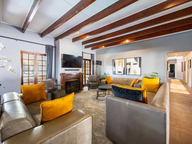 Spacious living room featuring exposed timber ceiling beams, a central fireplace, parquet flooring, and direct access to the garden through timber-framed french doors.