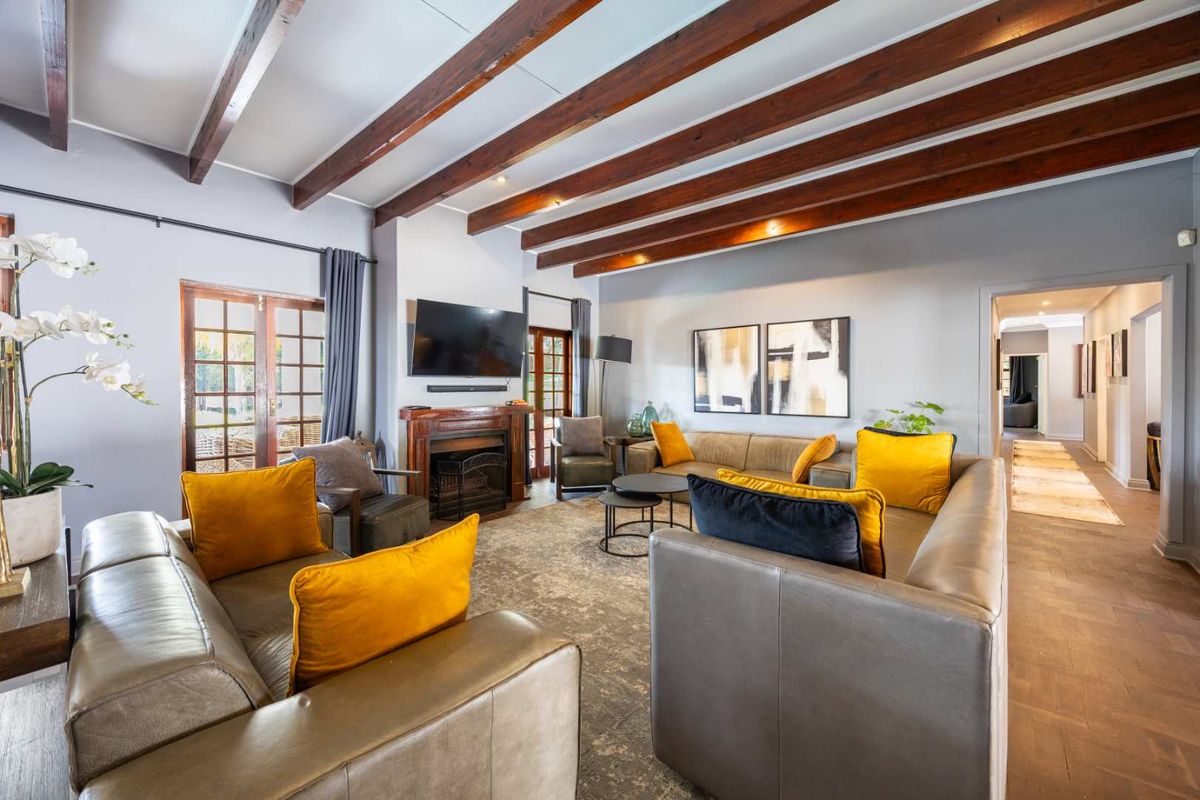 Spacious living room featuring exposed timber ceiling beams, a central fireplace, parquet flooring, and direct access to the garden through timber-framed french doors.
