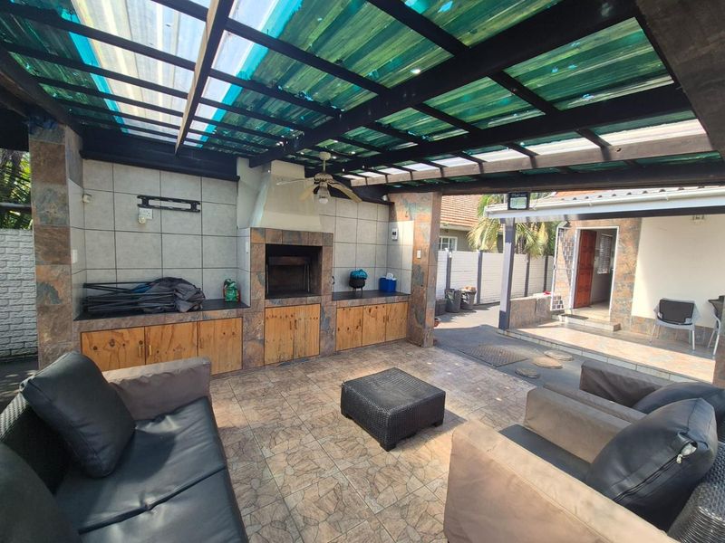 Covered outdoor patio area featuring a built-in braai, tiled flooring, and a timber pergola structure with translucent roofing.