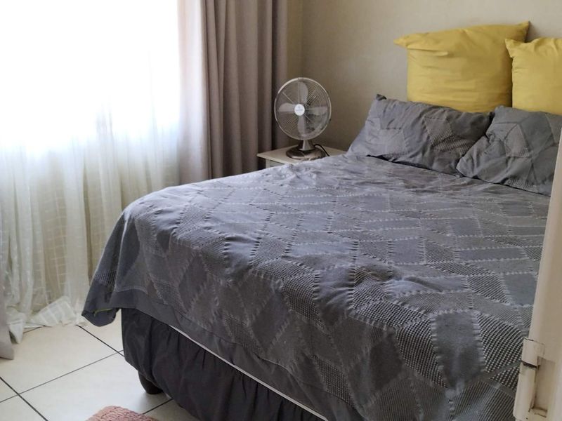 A functional bedroom featuring tiled flooring and natural light from a window with curtains.
