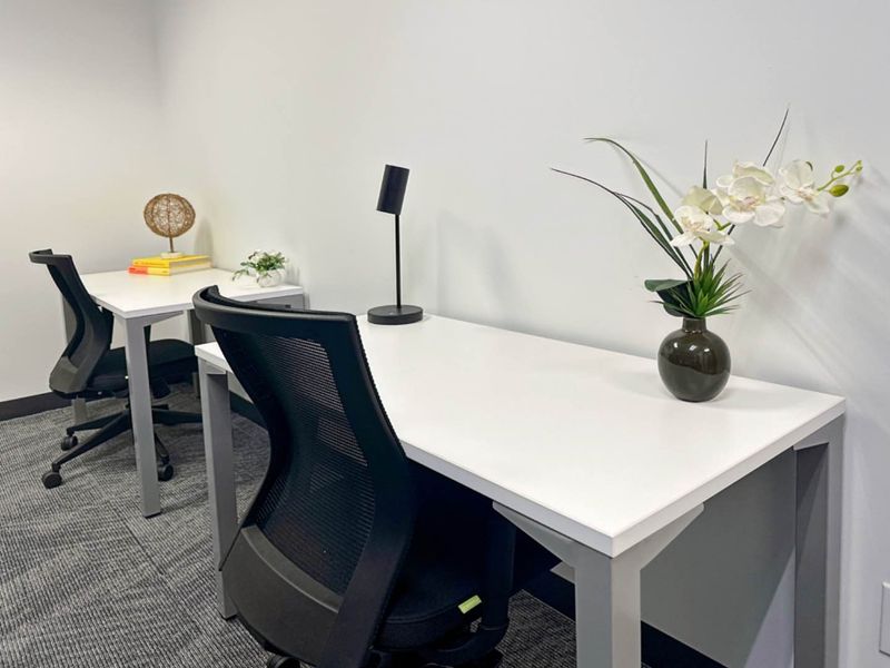A clean and modern office space featuring neutral walls, carpeted flooring, and functional workspace arrangements.