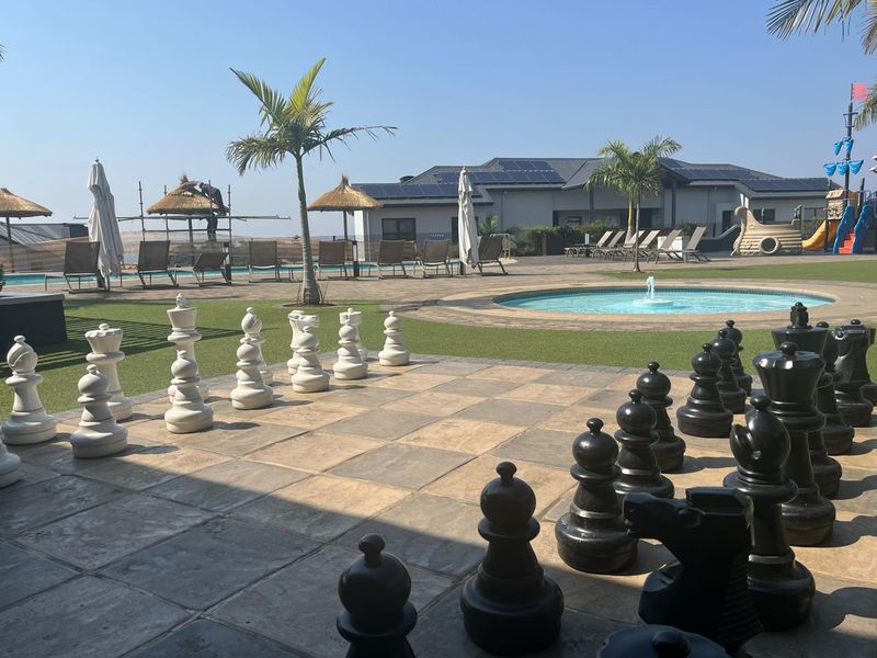 Outdoor recreational area featuring a swimming pool, water fountain, and a large paved giant chess board set within a landscaped garden.