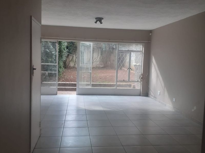An empty, open-plan living area featuring neutral tiled flooring and large glass doors providing direct access to the rear garden area.