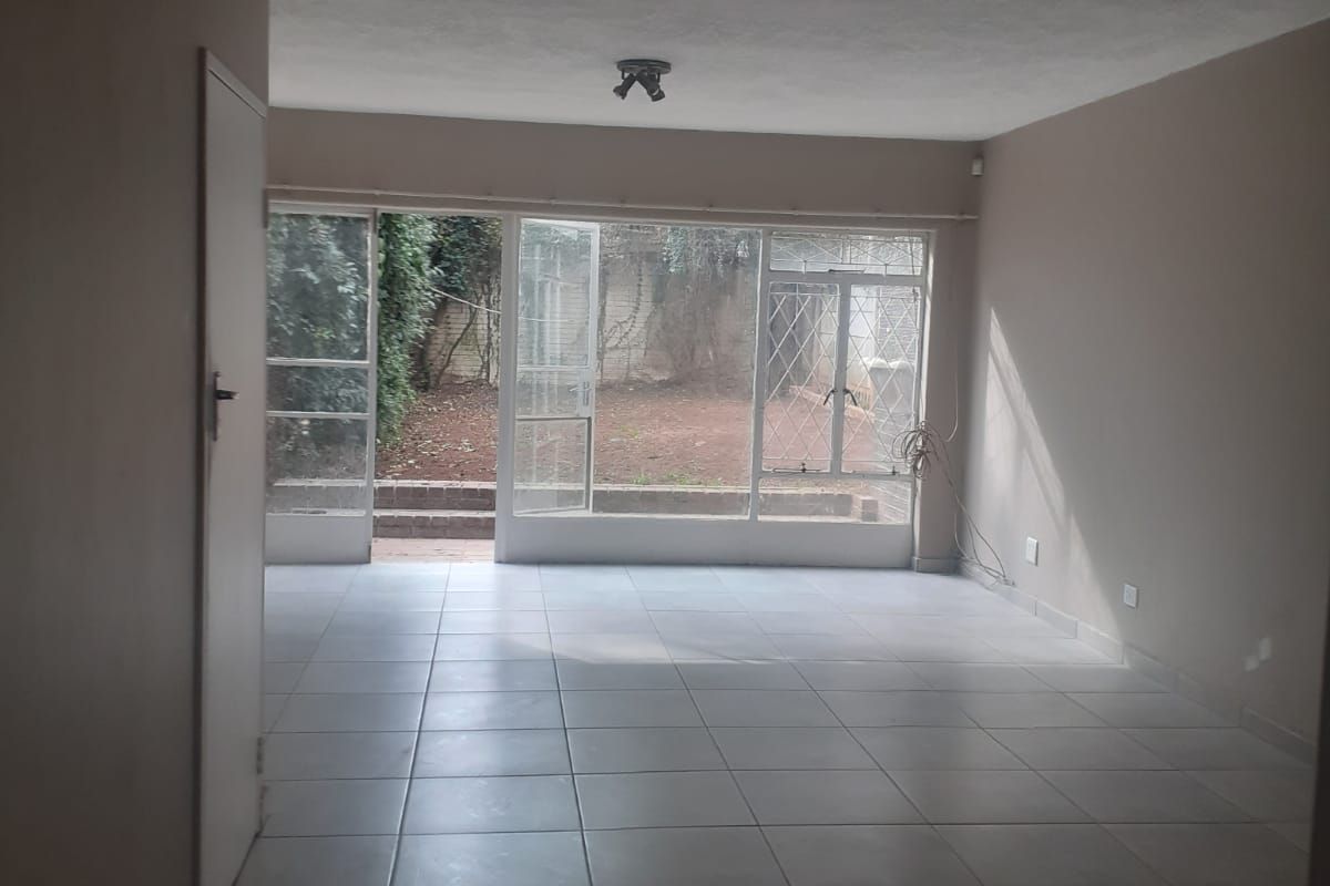 An empty, open-plan living area featuring neutral tiled flooring and large glass doors providing direct access to the rear garden area.