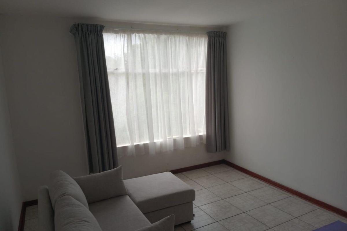 A simple living room featuring neutral tiled flooring and large windows with installed curtain tracks, offering a blank canvas for personalization.