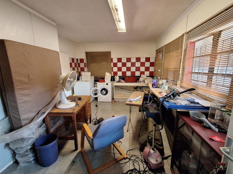 A functional laundry room featuring tiled splashbacks, tiled flooring, and ample natural light through venetian blinds.