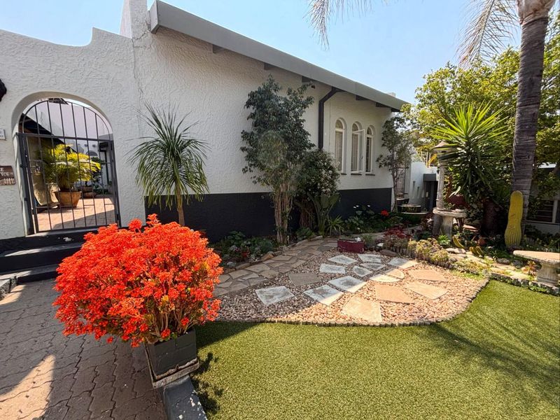 A well-maintained rear garden area featuring a stone pathway, artificial lawn, and an arched metal gate leading to a private courtyard.