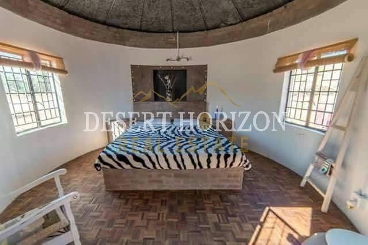A circular bedroom featuring parquet flooring, large windows with bamboo blinds, and a unique domed ceiling structure.