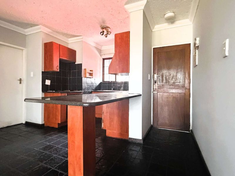 An empty kitchen featuring wooden cabinetry, a granite breakfast bar, and dark tiled flooring, offering a functional layout ready for modernization.