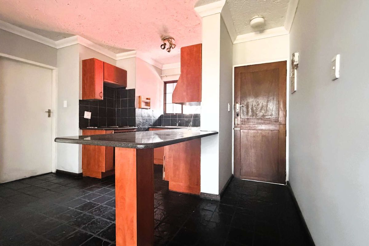 An empty kitchen featuring wooden cabinetry, a granite breakfast bar, and dark tiled flooring, offering a functional layout ready for modernization.