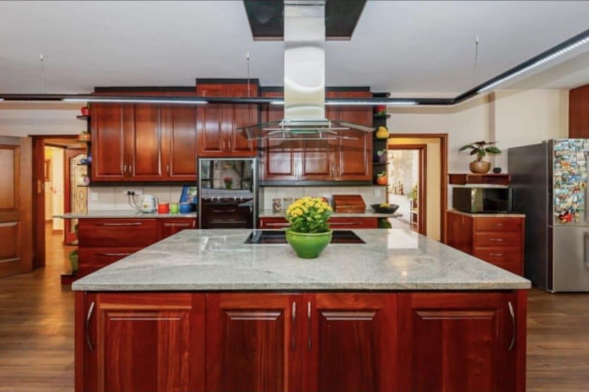 Spacious kitchen featuring rich wood cabinetry, a large central island with a stone countertop, and a modern stainless steel extractor fan.