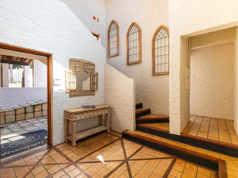 Spacious entrance hall featuring terracotta tile flooring, exposed brick walls, and unique arched windows leading to the staircase.