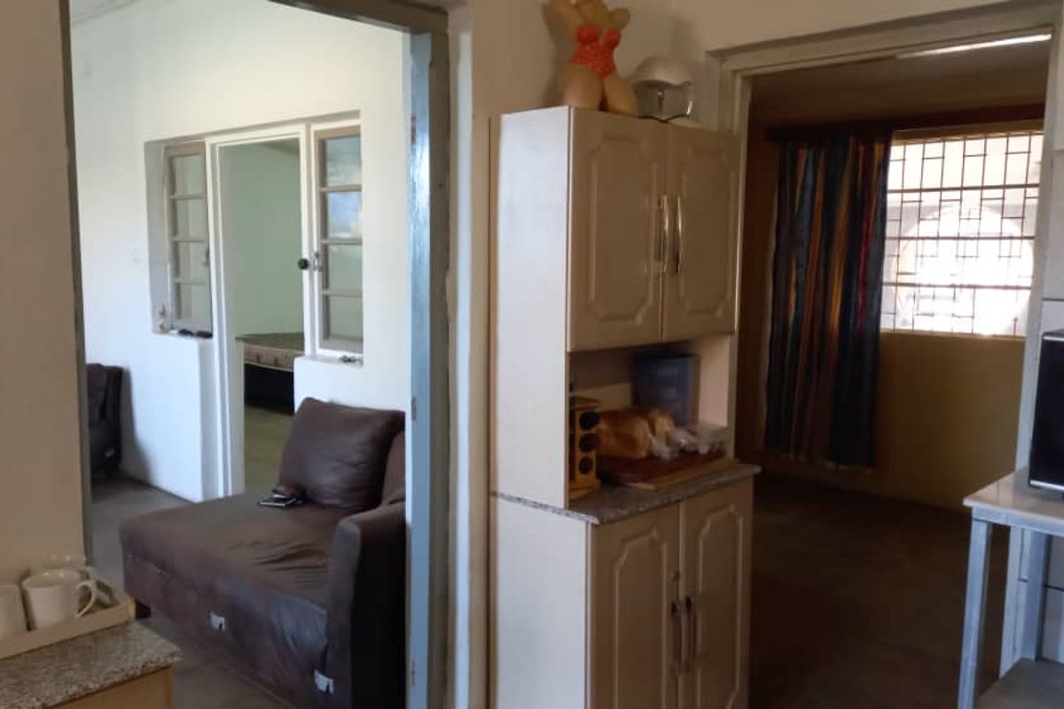 Interior view showing a kitchen area with built-in cabinetry, leading through to an adjacent living space with security bars on the windows.