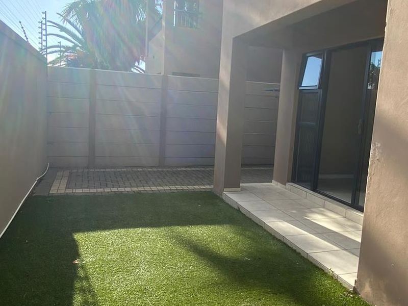 A private rear courtyard featuring a paved patio, artificial lawn, and secure boundary walling, accessible via a sliding glass door.
