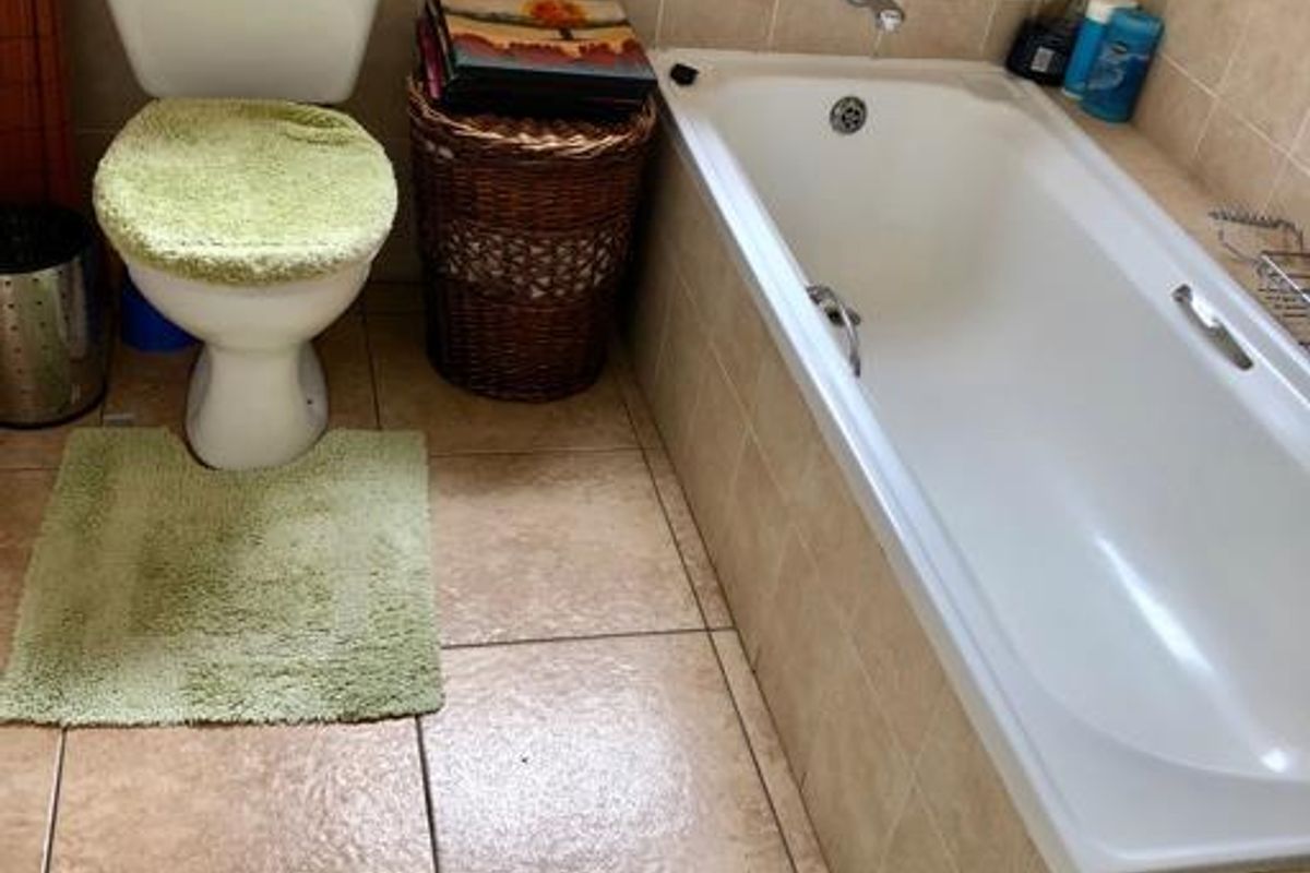 A functional bathroom featuring a built-in bathtub with tiled surround and a standard toilet, finished with neutral ceramic floor and wall tiles.