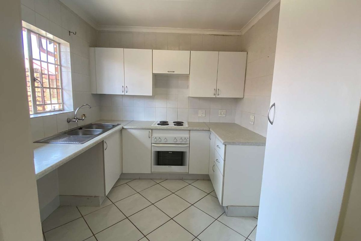A functional kitchen featuring white cabinetry, a built-in oven and hob, tiled flooring, and a double sink with a window view.