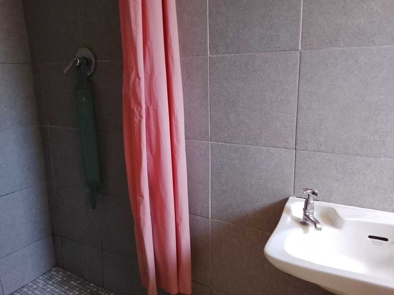 A functional bathroom featuring a wall-mounted basin with chrome tapware and a tiled shower enclosure with mosaic flooring.