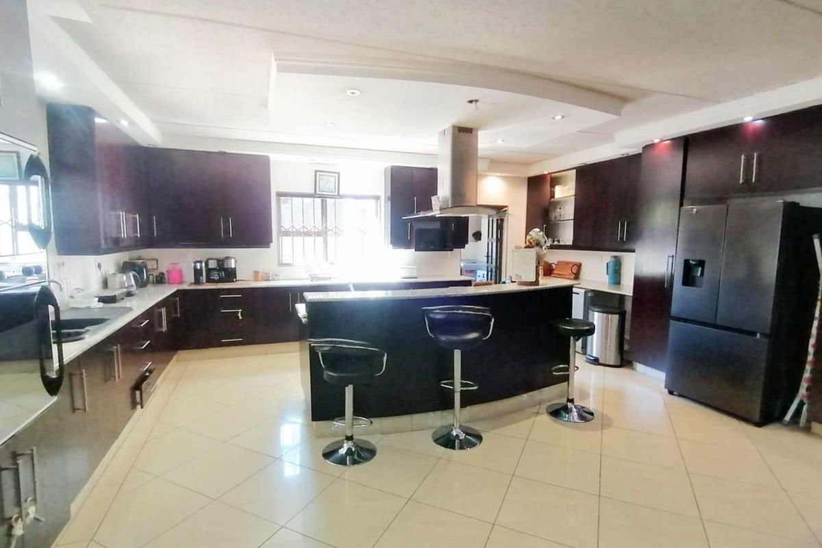 Spacious kitchen featuring dark wood cabinetry, granite countertops, a central island with breakfast bar seating, and modern recessed ceiling lighting.