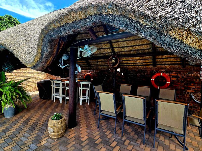 A covered outdoor patio area featuring a traditional thatched roof, exposed brick walls, and durable brick paving, ideal for relaxed outdoor entertaining.