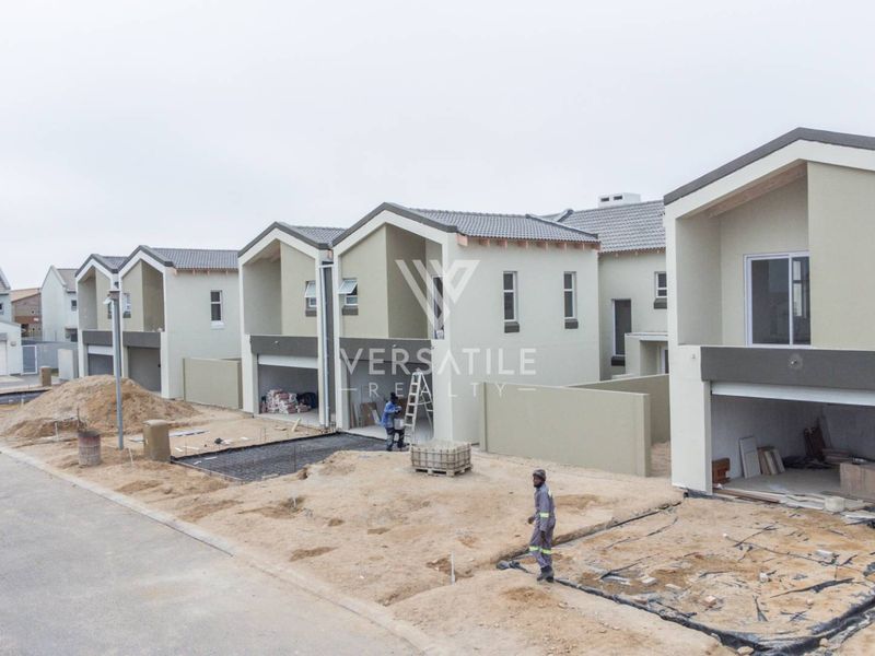 Aerial view of a townhouse development under construction, featuring multiple units with garages, tiled roofs, and ongoing site work.