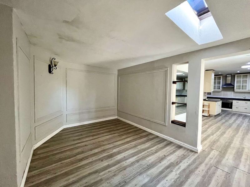 An open-plan living area featuring laminate flooring, decorative wall molding, a skylight, and a pass-through window connecting to the kitchen.