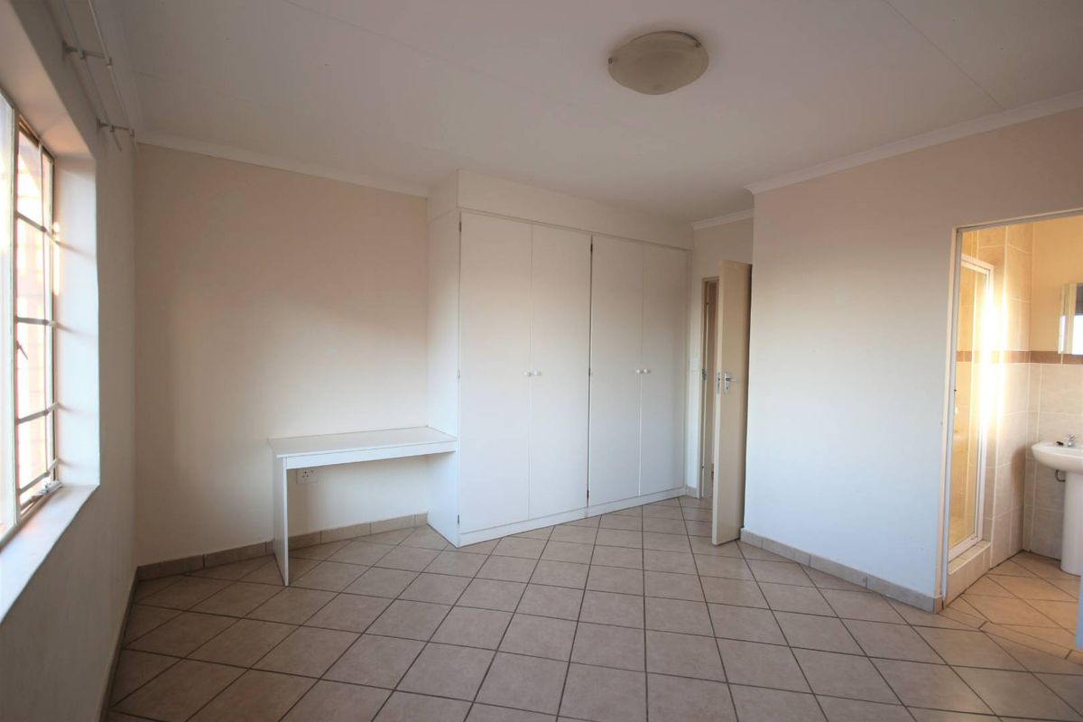 A spacious, empty bedroom featuring tiled flooring, built-in cupboards, a built-in desk, and an en-suite bathroom entrance.