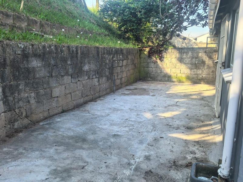 A rear exterior area featuring a concrete paved surface enclosed by a weathered concrete block retaining wall.