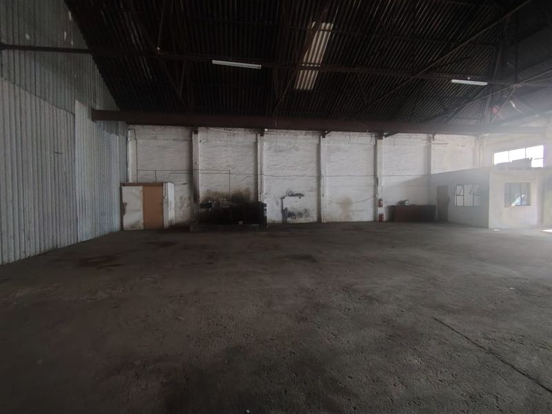 Spacious industrial warehouse unit featuring high ceilings with exposed steel trusses, concrete flooring, and painted brick walls, suitable for storage or manufacturing operations.