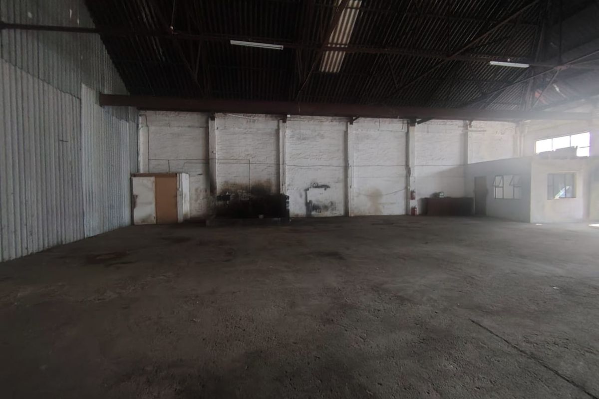 Spacious industrial warehouse unit featuring high ceilings with exposed steel trusses, concrete flooring, and painted brick walls, suitable for storage or manufacturing operations.