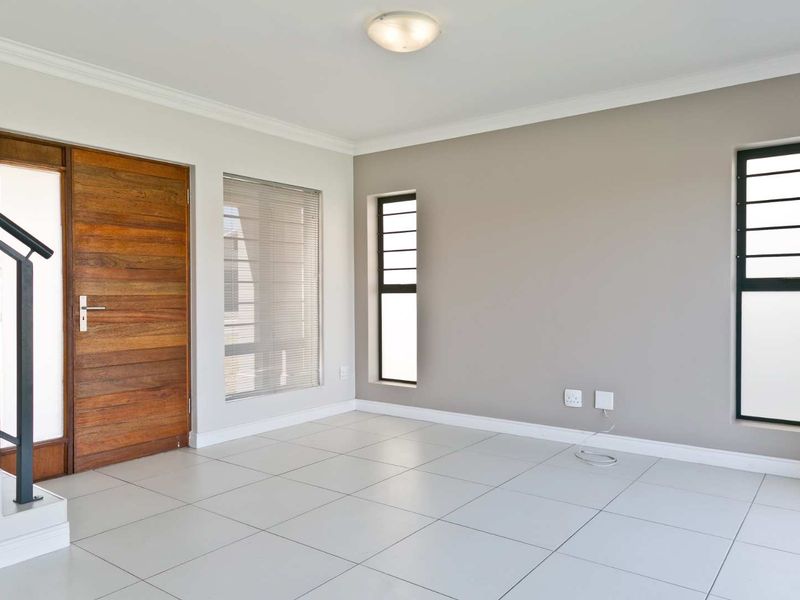 Bright and spacious entrance area featuring neutral tiled flooring, a solid wooden front door, and modern staircase access.