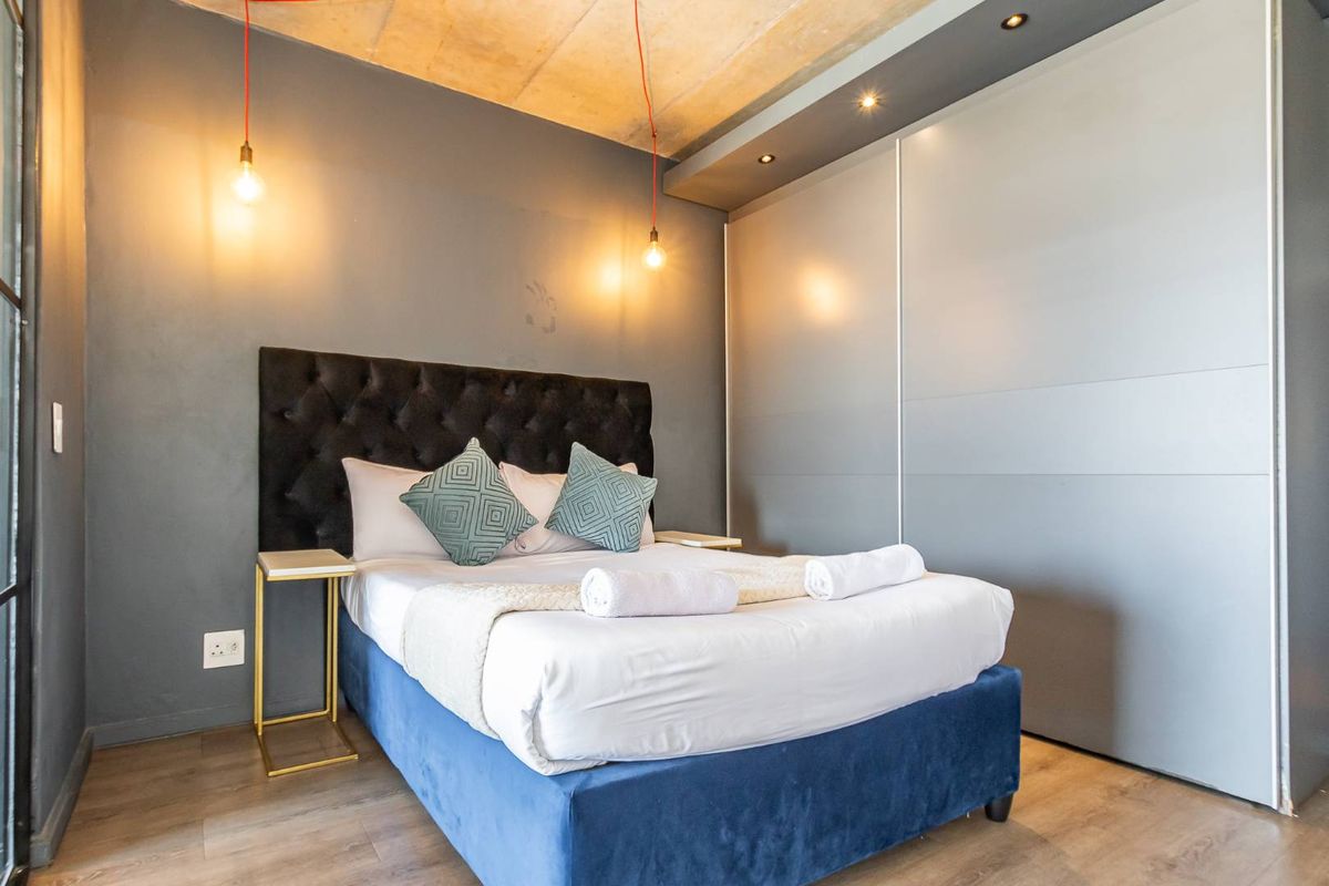 Modern bedroom featuring a raw concrete ceiling, built-in floor-to-ceiling sliding door wardrobes, and contemporary pendant lighting.