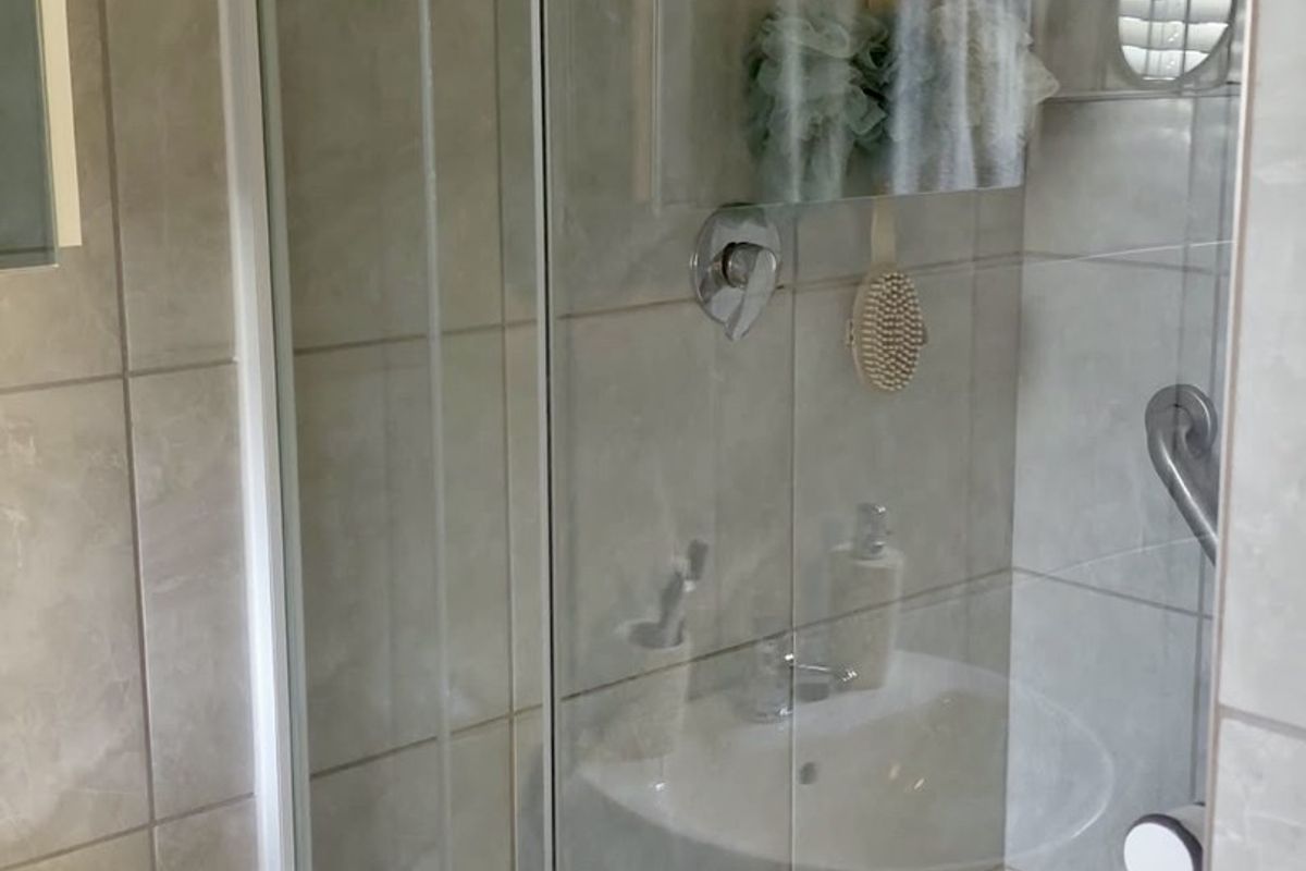 A functional bathroom featuring a glass-enclosed shower, neutral ceramic wall tiling, and a pedestal basin.