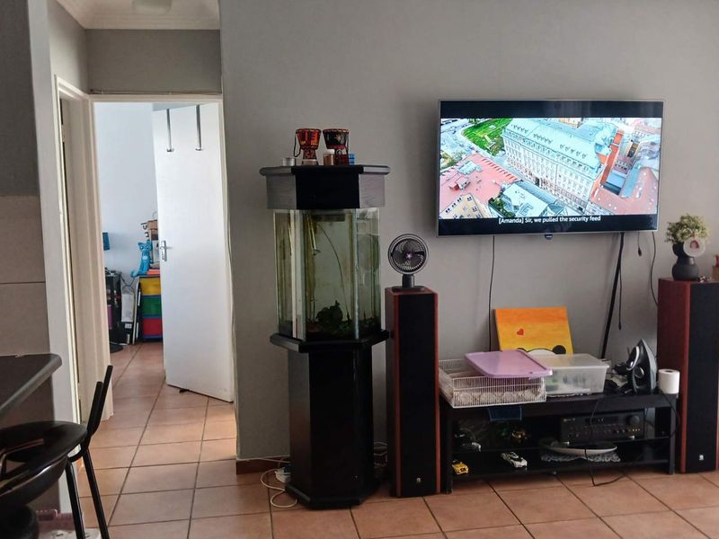 A living room area featuring tiled flooring and a wall-mounted television, with an adjacent doorway leading to another room.