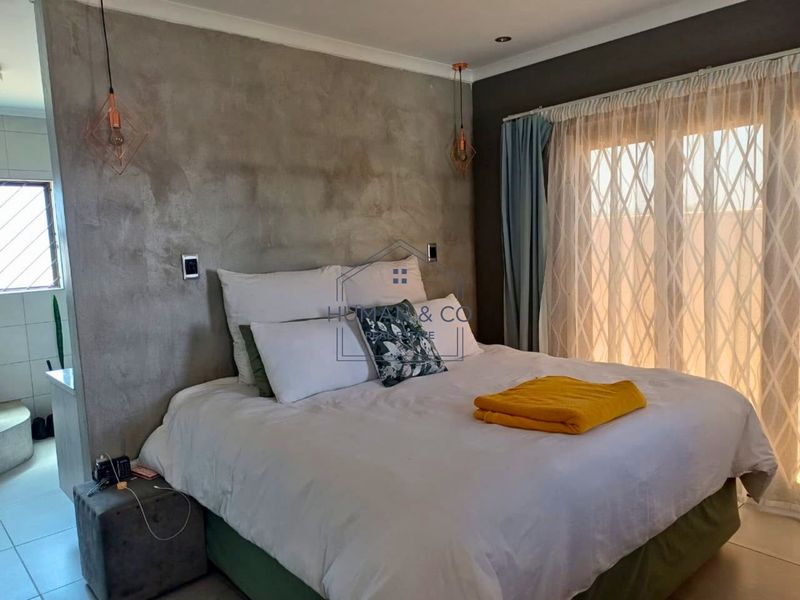 A modern bedroom featuring a textured cementitious feature wall, pendant lighting, and direct access to an outdoor area through a sliding glass door.