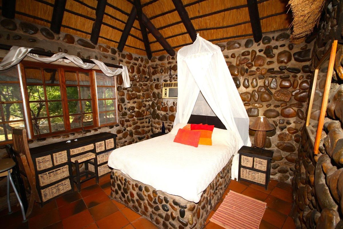 Rustic bedroom featuring distinctive natural stone walls, exposed timber roof beams, thatched ceiling, and terracotta floor tiles with a built-in stone bed base.