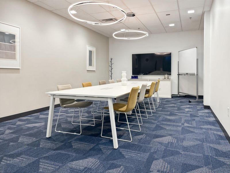 A modern, well-maintained office meeting room featuring patterned carpet tiles, suspended ceiling with recessed lighting, and integrated cabinetry.