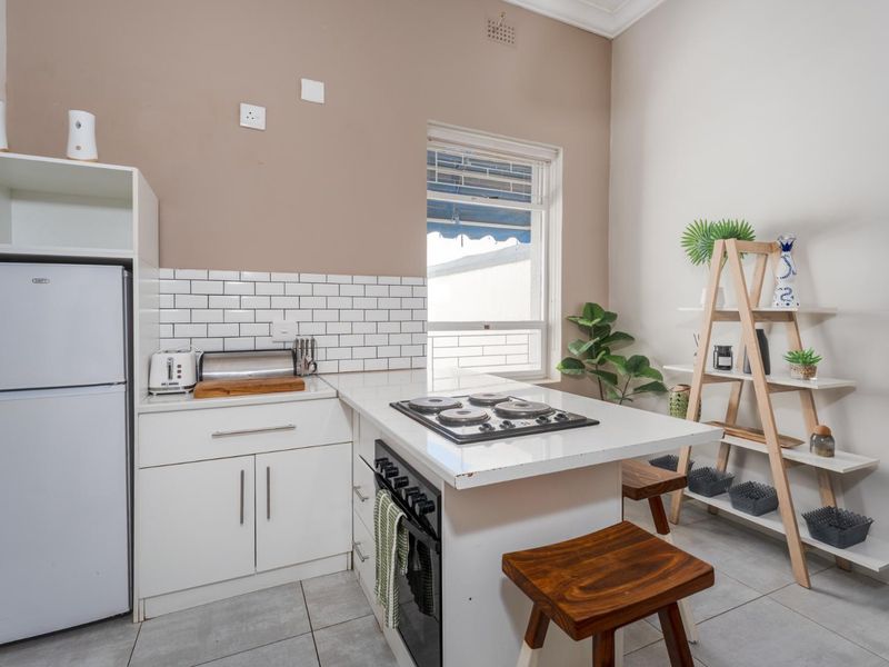 Compact kitchen featuring white cabinetry, subway tile backsplash, integrated electric hob and oven, and tiled flooring.