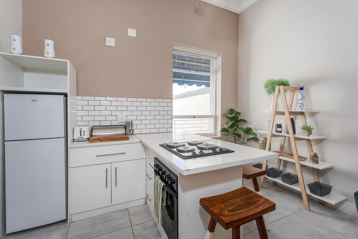 Compact kitchen featuring white cabinetry, subway tile backsplash, integrated electric hob and oven, and tiled flooring.