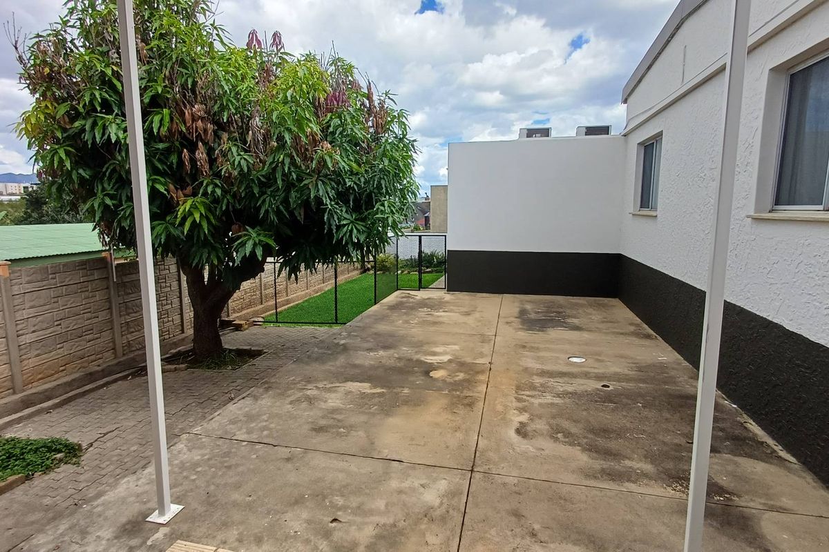 A paved rear outdoor area featuring a large tree, perimeter walling, and direct access to the main dwelling structure.