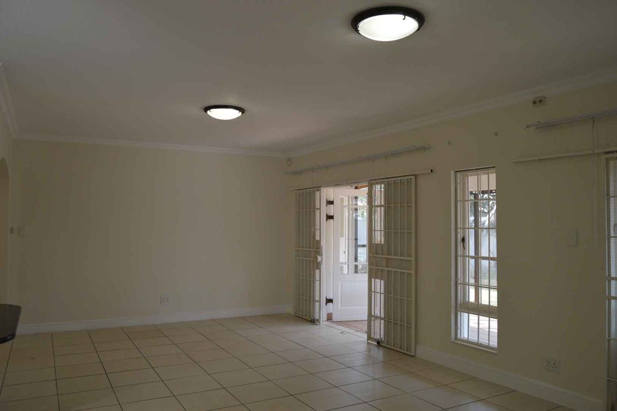 A spacious, empty living area featuring neutral tiled flooring, flush mount lighting, and security gates leading to the exterior.