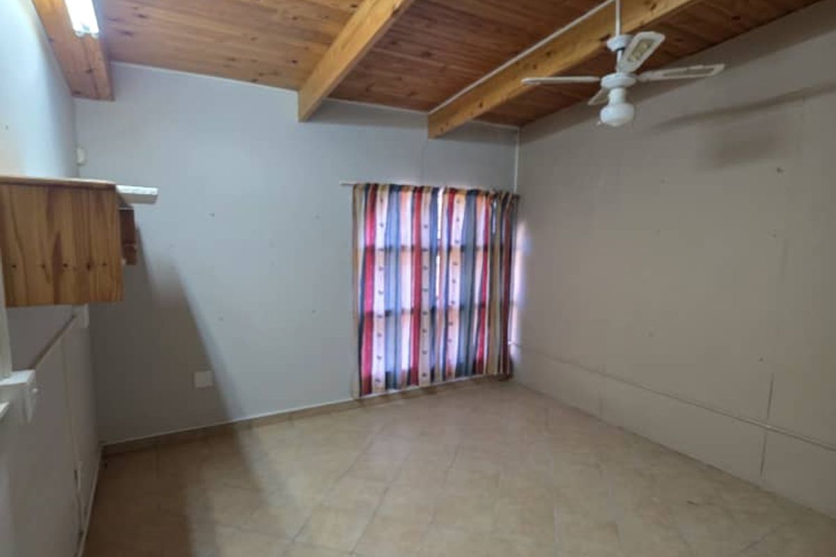 A spacious bedroom featuring a high vaulted timber-beamed ceiling, tiled flooring, and a ceiling fan, offering a blank canvas for personalization.