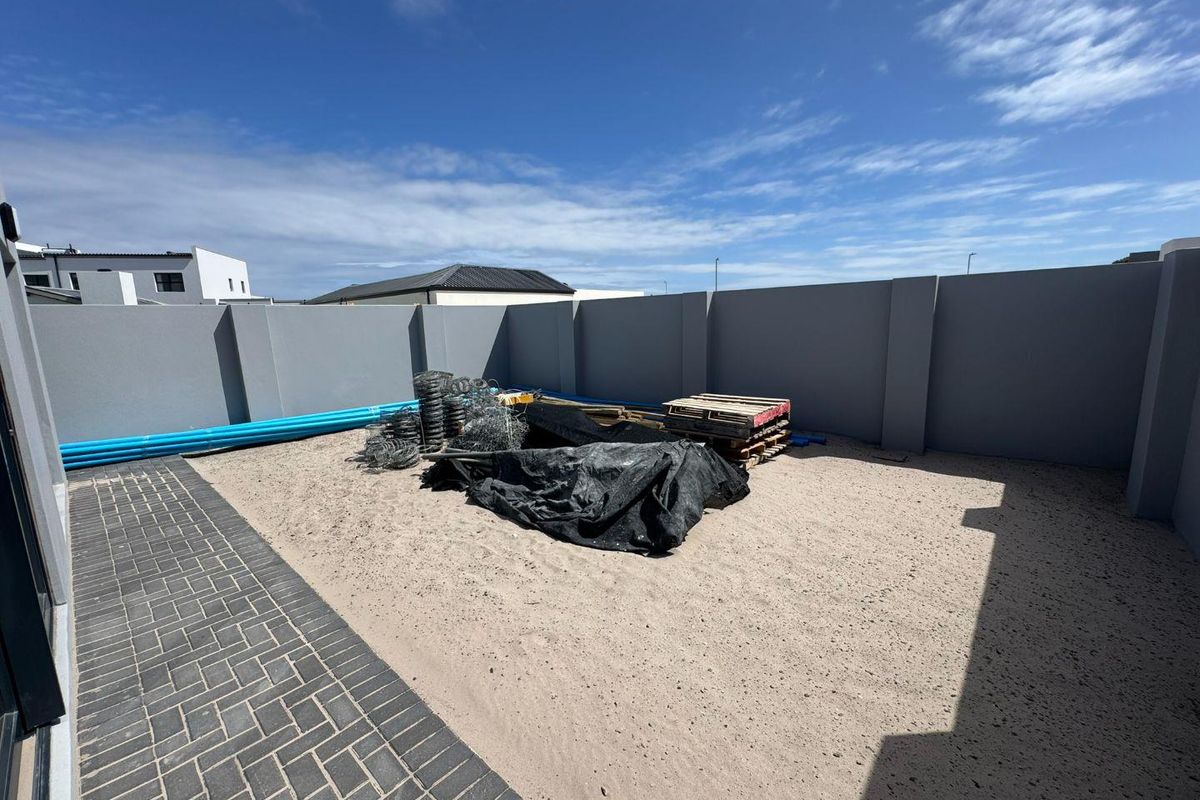 An undeveloped rear garden area featuring perimeter boundary walls and paved walkway, currently awaiting landscaping and final finishing.