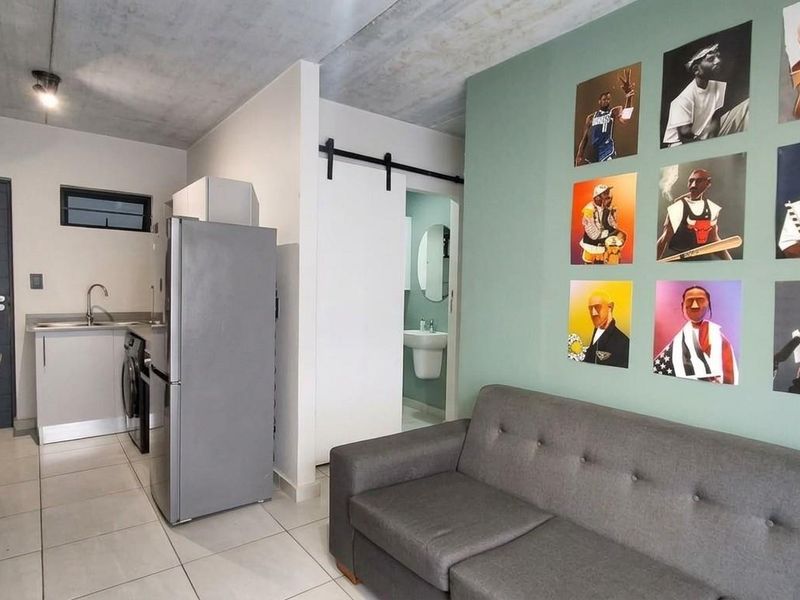 Open plan living area featuring a compact kitchen with modern cabinetry, tiled floors, and an exposed concrete ceiling, leading to a separate bathroom.