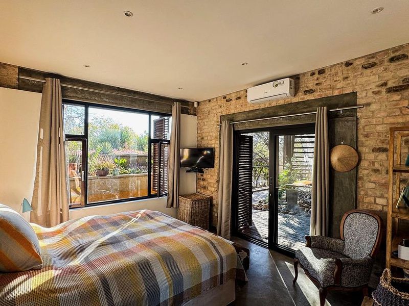 A cozy bedroom featuring exposed brick walls, concrete flooring, and large sliding glass doors that provide direct access to the outdoor garden area.