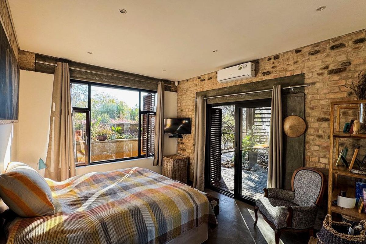 A cozy bedroom featuring exposed brick walls, concrete flooring, and large sliding glass doors that provide direct access to the outdoor garden area.