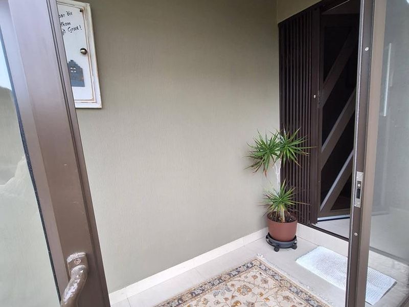 A clean and well-maintained entrance area featuring tiled flooring and a modern slatted privacy screen, accessed through a sliding glass door.